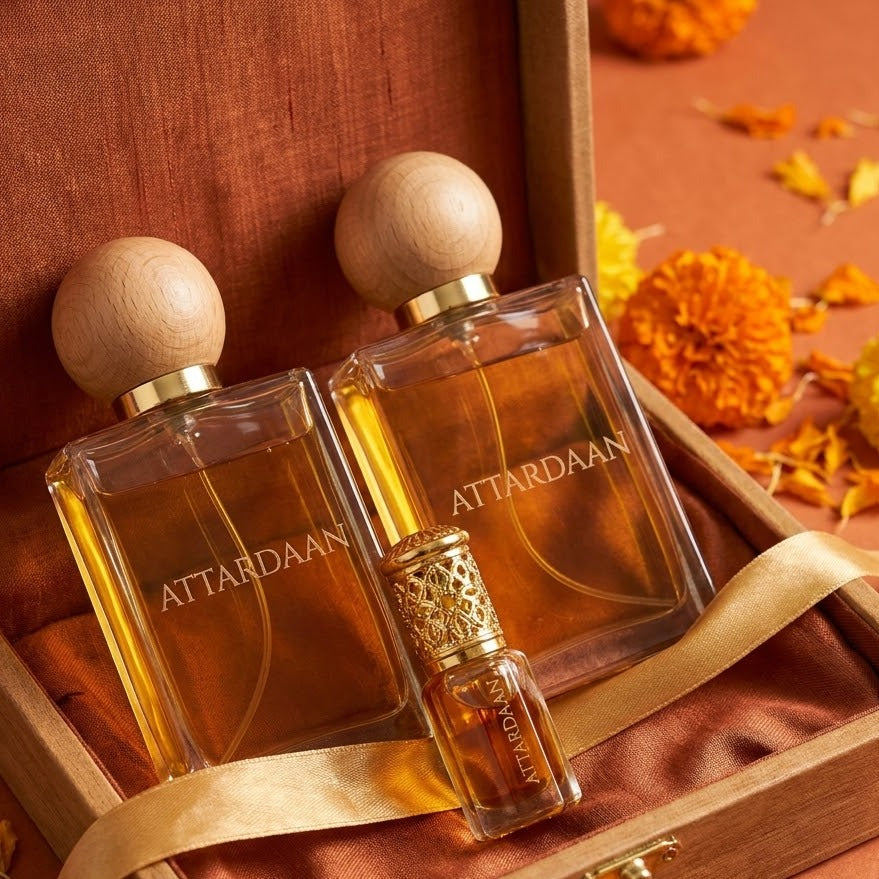 Rutbaa big brother splurge set — two large Attardaan eau de parfum bottles and a gold-capped attar vial in a wooden presentation box on rust silk with marigolds
